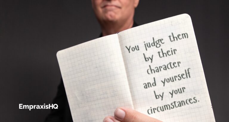 Tim Miles holding an open pocket notebook, on which is written "You judge them by their character and yourself by your circumstances."