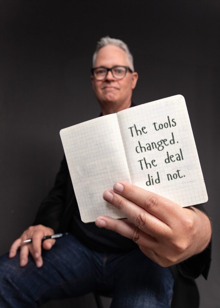 Tim Miles holding an open pocket notebook, on which is written "The tools changed. The deal did not."